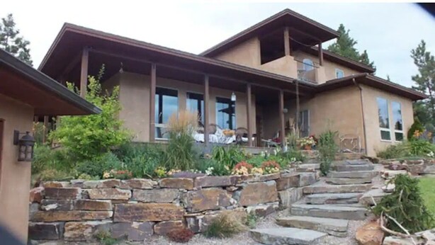 A two-story house with a stone retaining wall, a covered porch, and a landscaped garden. - Montana Mountaintop Ranch Estate (Proctor)