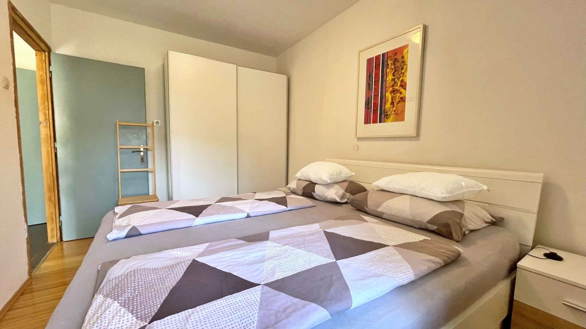Un dormitorio con cama, almohadas, mesita de noche, un cuadro en la pared y una puerta.