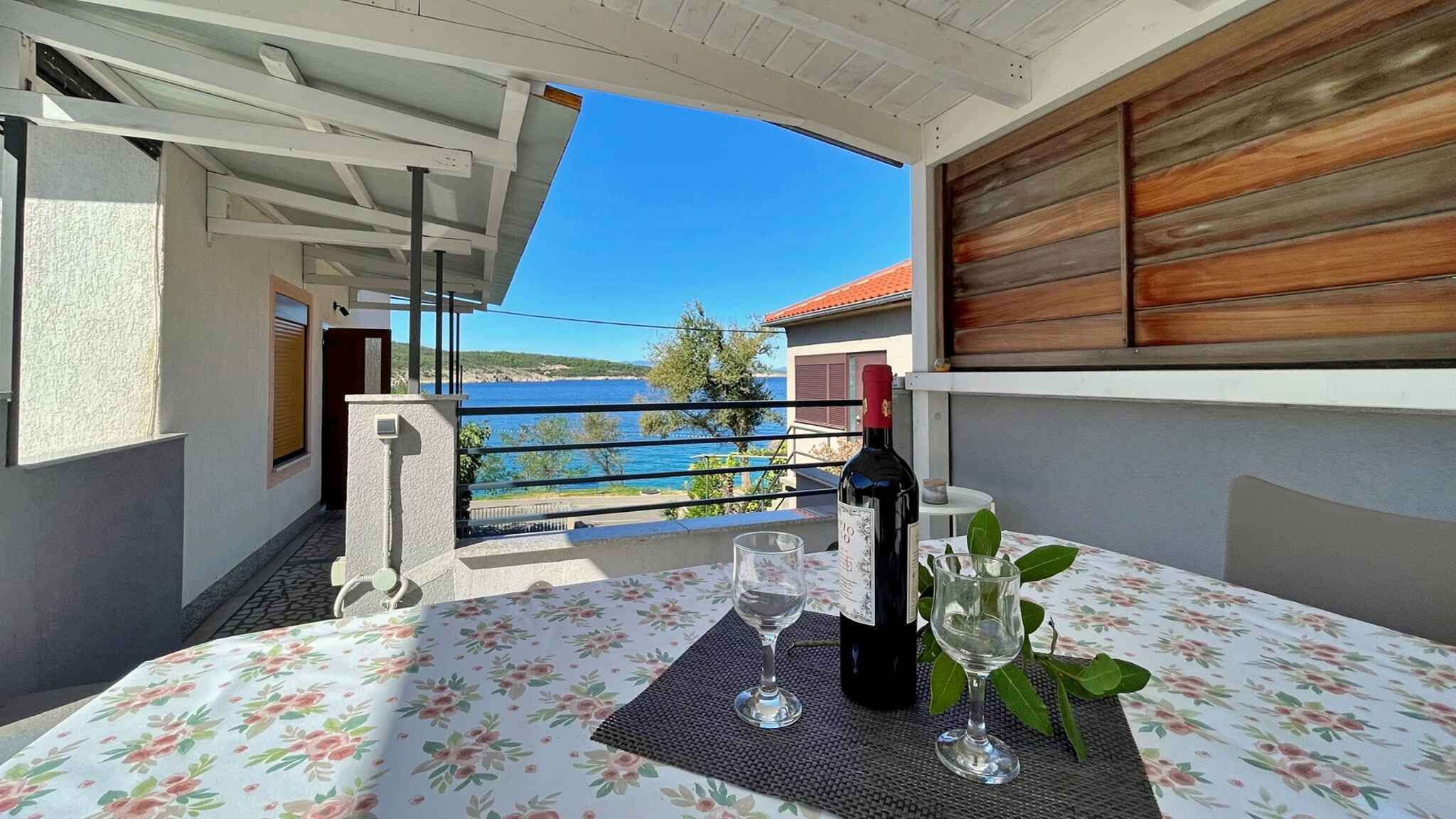 Ein Balkon mit Tisch für zwei Personen, mit Blick auf eine schöne Meerlandschaft und ein Gebäude.