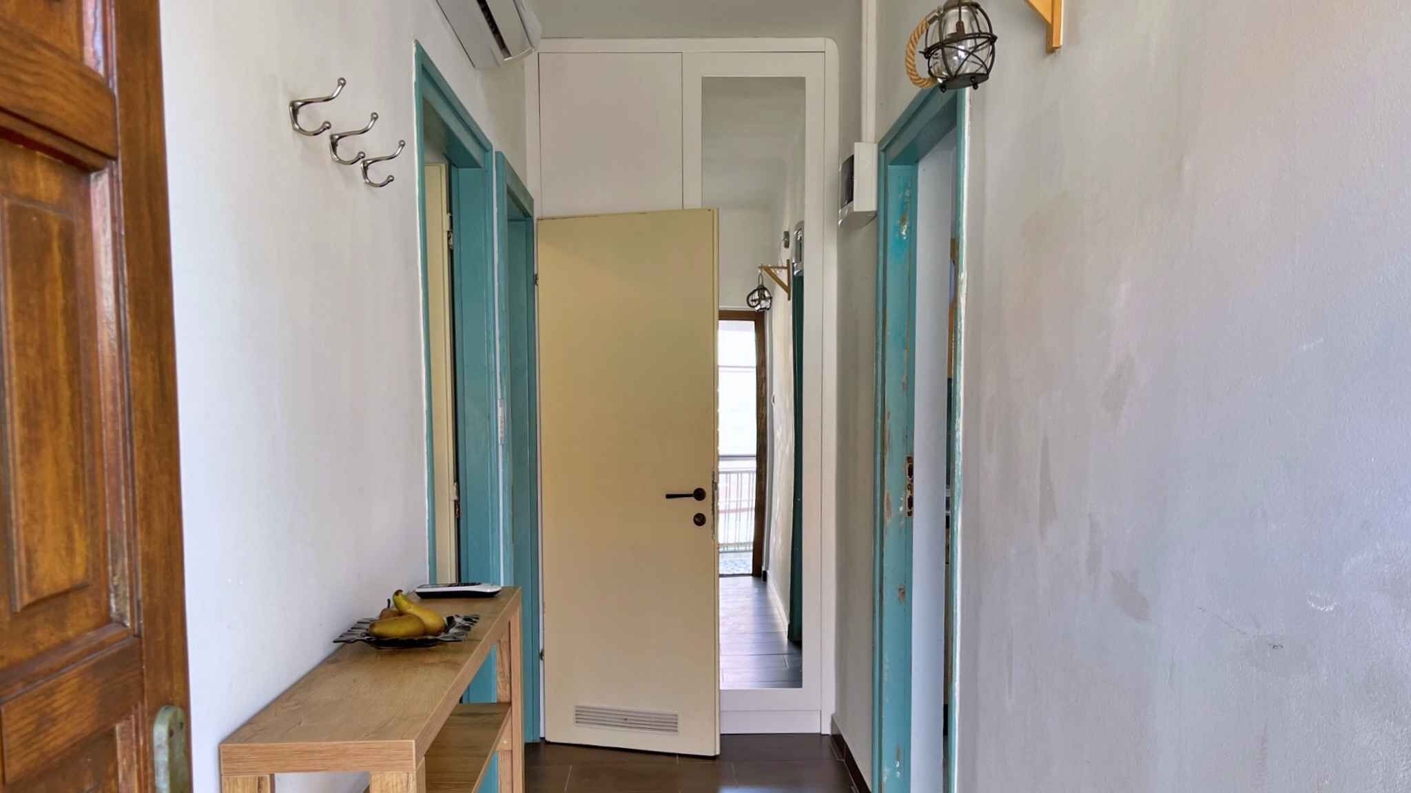 Un pasillo estrecho con un banco de madera, una puerta y una lámpara fijada a la pared.