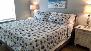 A bedroom with a bed, two bedside lamps, a painting on the wall, and a window. - Beach Cove: Ocean Front 4Bed/2Bath - Ocean City MD (Ocean City)