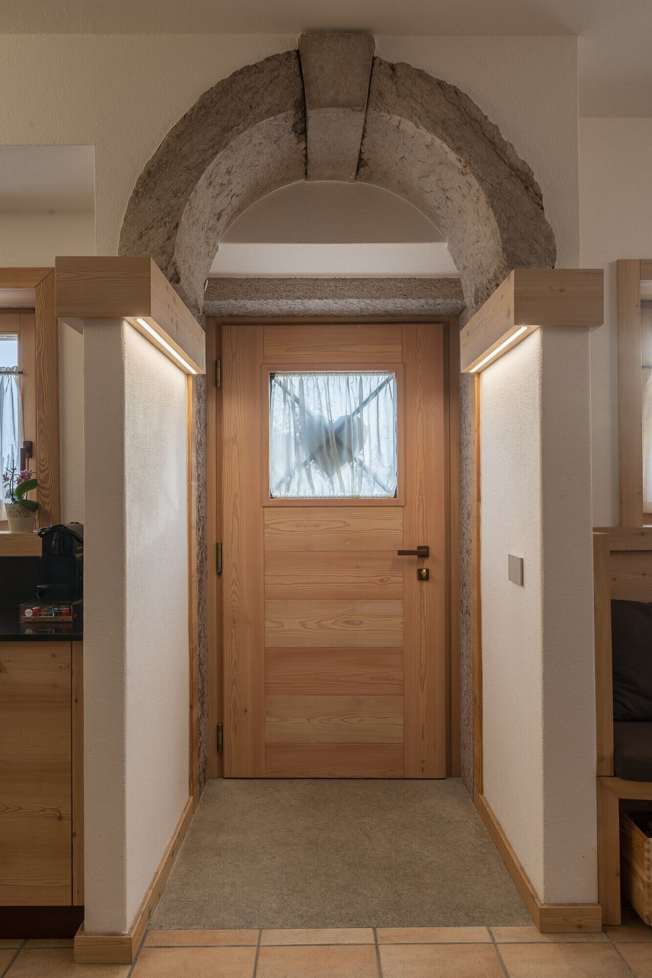 A wooden door with a frosted glass window, flanked by wooden walls and a stone archway.