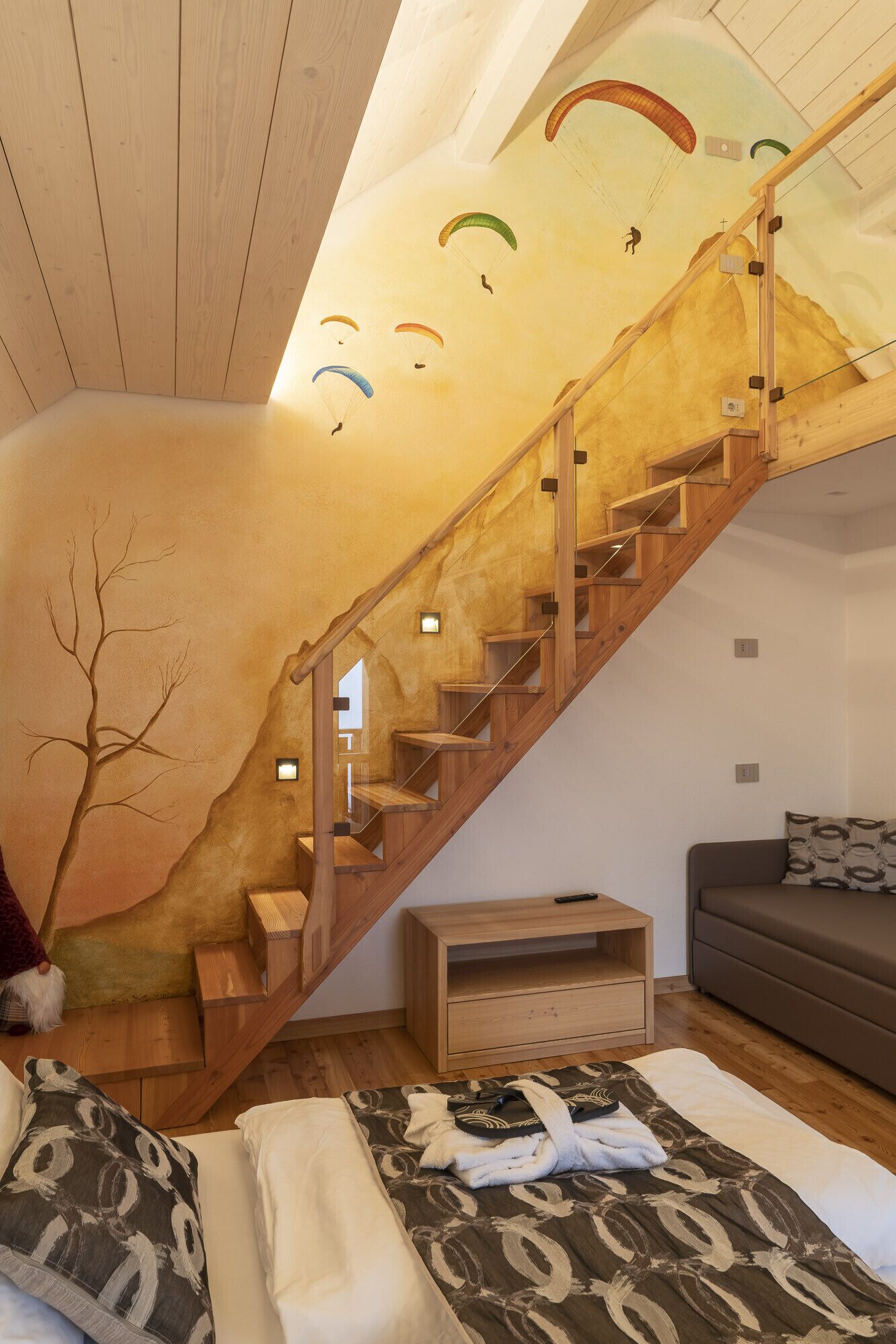 Ein Schlafzimmer mit einer Holztreppe, einem Bett mit gemusterten Textilien, einem Nachttisch und einem Sofa.