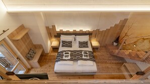 Een kamer met houten wanden, een schuin dak en een bed in het midden, met hoge plafonds.