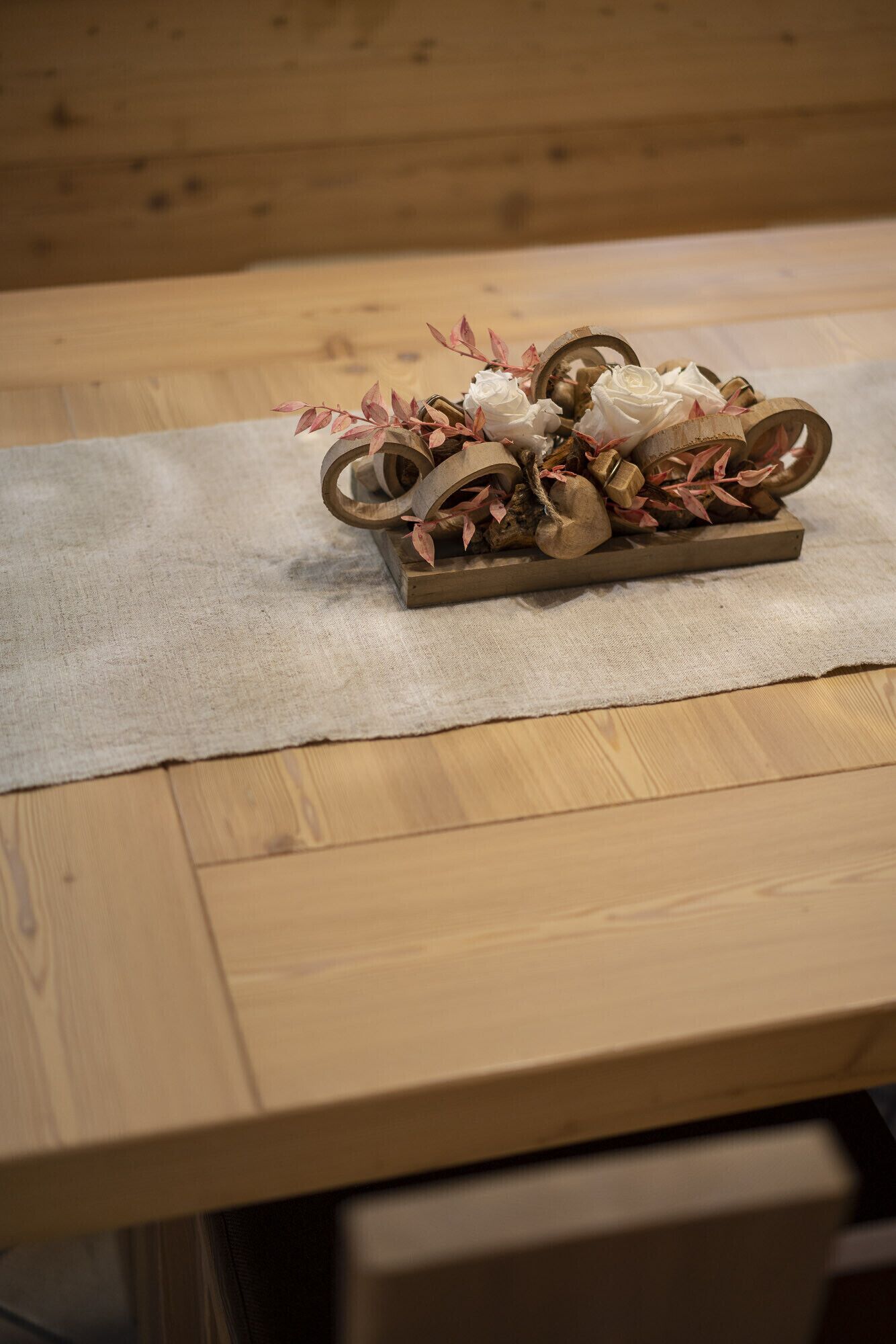 A wooden table with a rectangular tray holding decorative items like flowers and leaves.