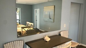 Un comedor con una mesa de madera oscura, dos sillas blancas y un espejo grande que refleja la habitación.