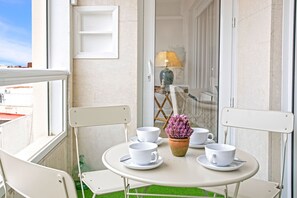 A small outdoor seating area with a round table, white chairs, and a potted plant.