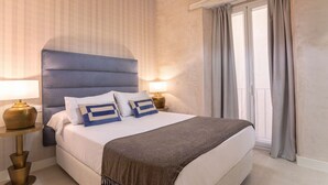 A neatly made bed with a blue headboard, two bedside lamps, and a window with curtains. - Genteel Home Feria II (Sevilla)