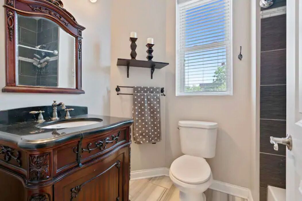 A bathroom with a wooden vanity, a mirror, a toilet, and a window with blinds.