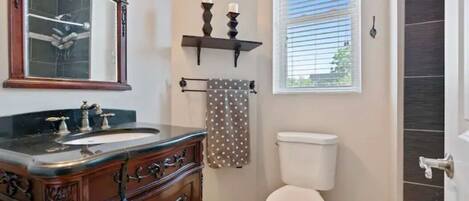 A bathroom with a wooden vanity, a mirror, a toilet, and a window with blinds.