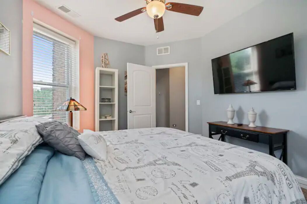 A bedroom with a bed, a ceiling fan, a TV, a wardrobe, and a bedside table.