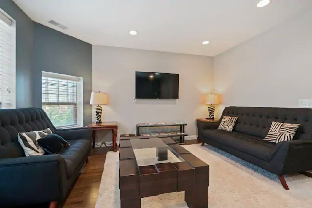 A living room with a dark-colored sofa, a coffee table, and a flat-screen TV mounted on the wall.