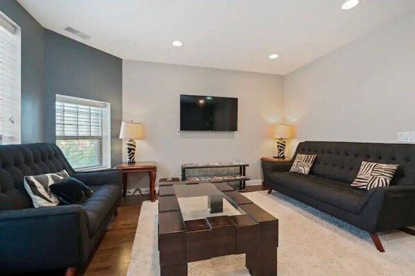 A living room with a dark-colored sofa, a coffee table, and a flat-screen TV mounted on the wall.