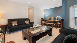 En moderne stue med en sort sofa, et glasbord og et spiseområde med et træbord og stole.