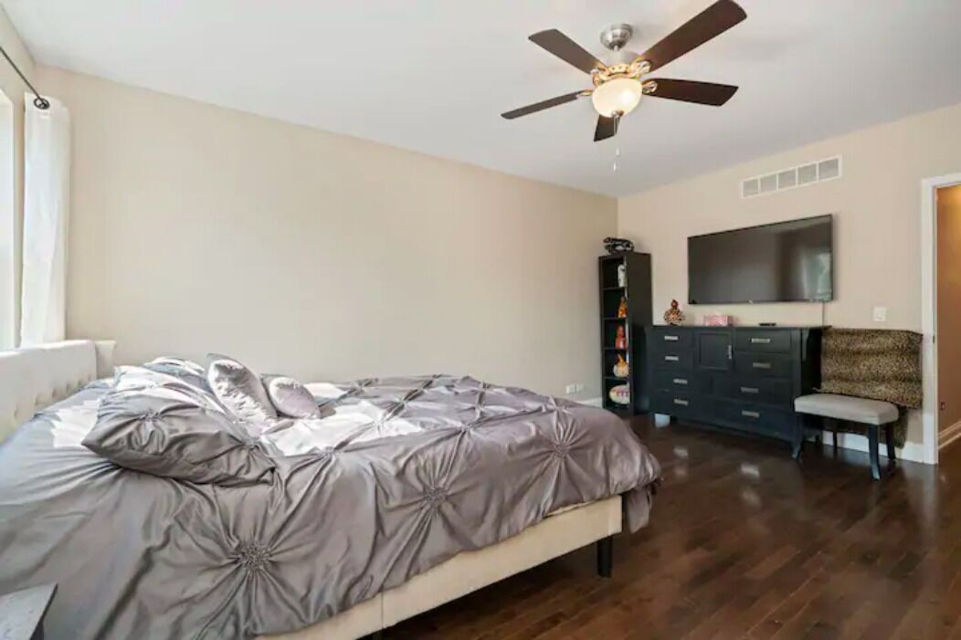 A bedroom with a bed, a ceiling fan, a dresser, and a TV mounted on the wall.