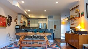 A modern kitchen with a wooden dining table, chairs, and a colorful rug.