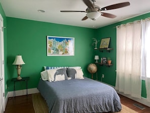 A bedroom with a bed, a ceiling fan, a globe, and a window with curtains.