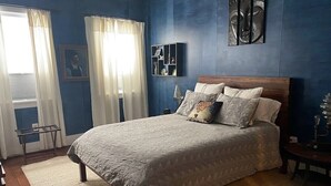 A bedroom with a large bed, a nightstand, a lamp, and a wall-mounted shelf.