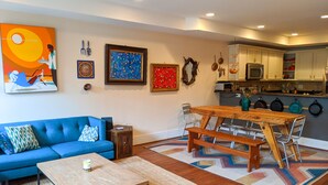 A modern living room with a blue sofa, a wooden coffee table, and a dining area with a wooden table and metal chairs.