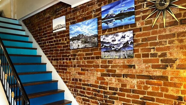 A staircase with blue steps leading to a brick wall adorned with framed landscape paintings.