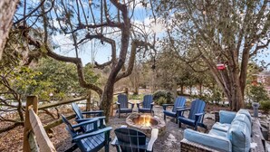 An outdoor seating area with Adirondack chairs and a fire pit surrounded by trees.