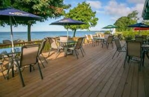 Een houten terras met buitenmeubilair, parasols en uitzicht op zee.