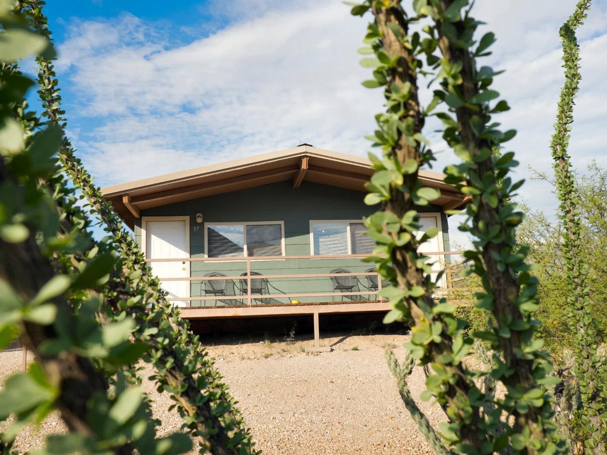 A single-story building with a sloped roof, a balcony, and a gravel driveway.