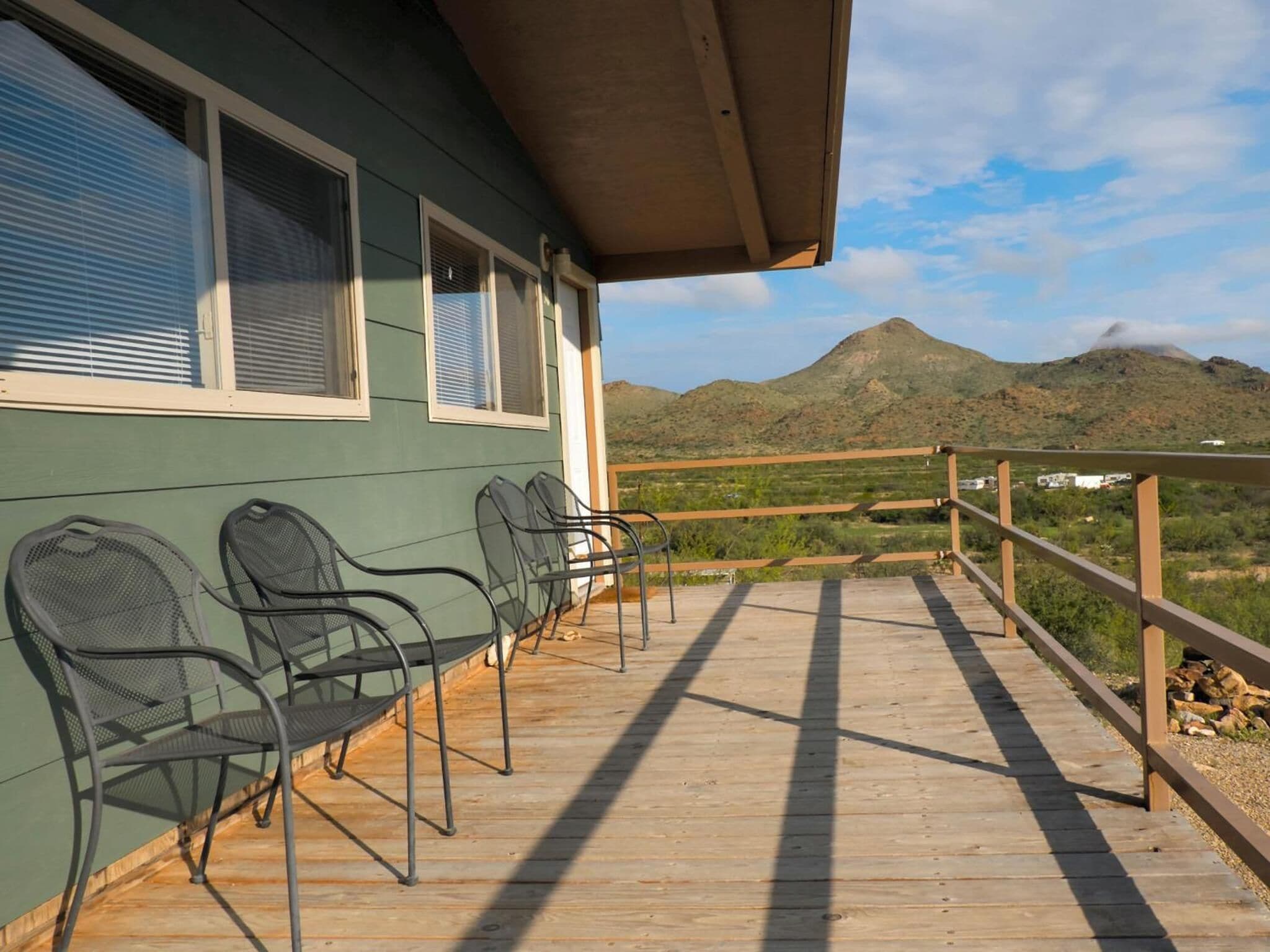 En træterrasse med metalstole, gelænder og udsigt til et bjerg.