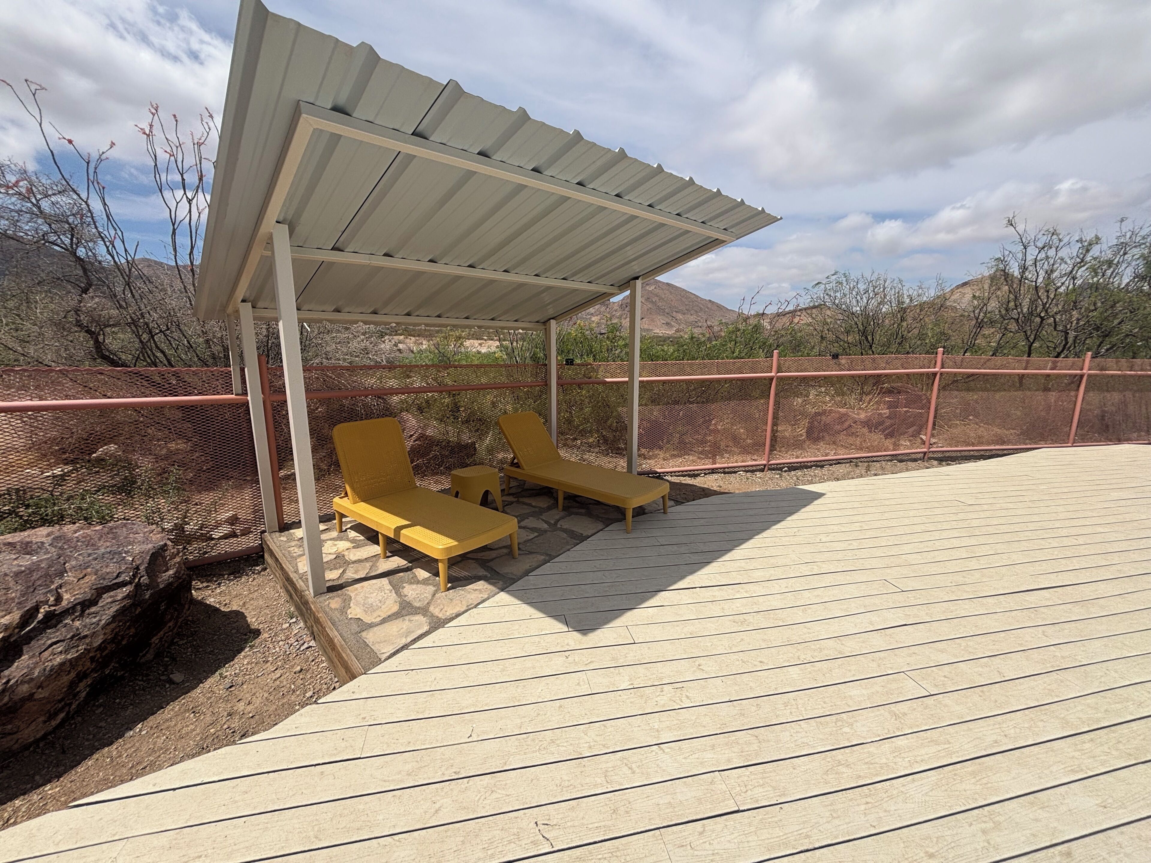Un área de estar al aire libre techada, con dos sillones amarillos y una terraza de madera.