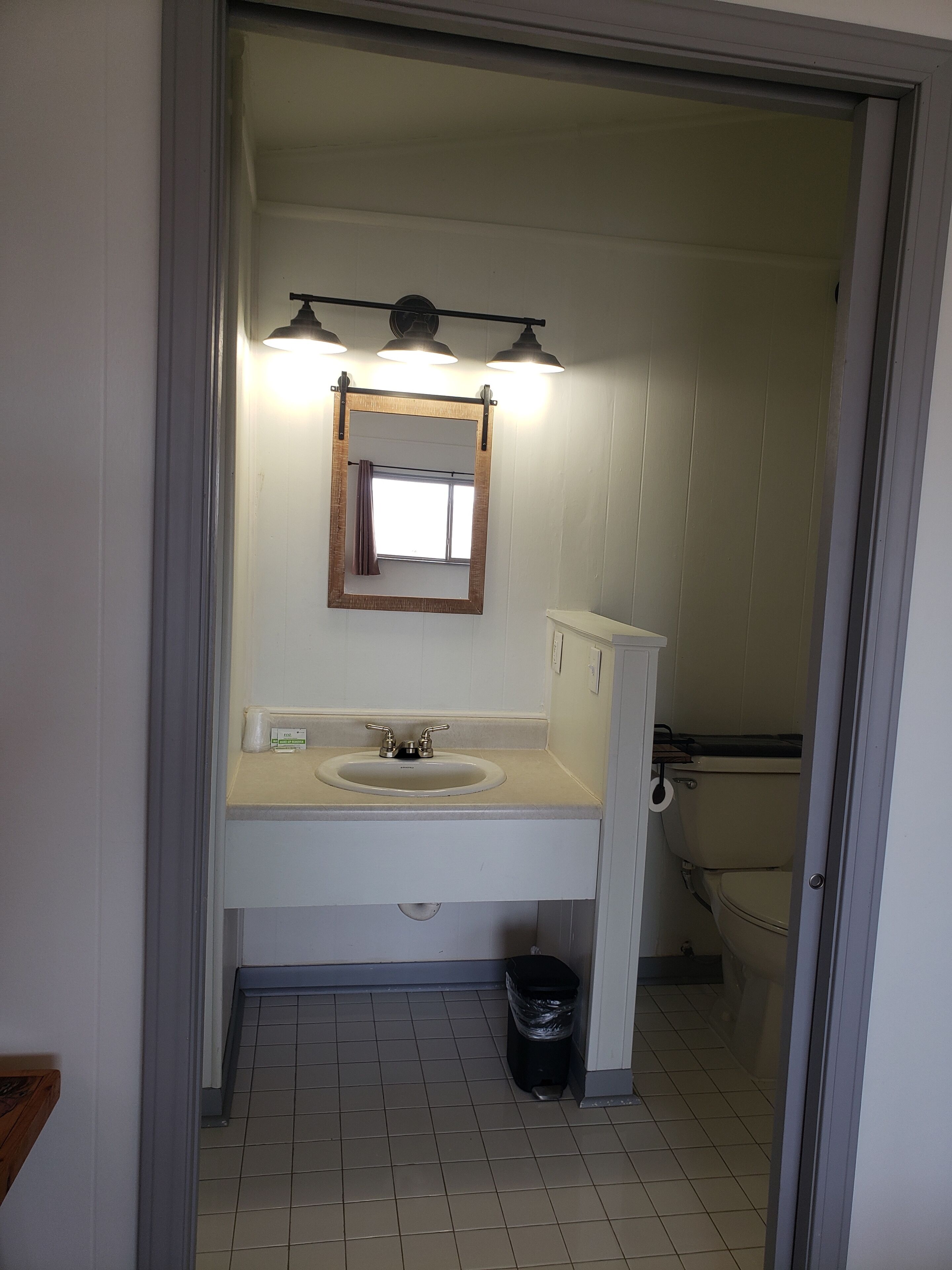 Une salle de bain avec un lavabo, un miroir et des toilettes. On y trouve une poubelle et une serviette accrochée au mur.