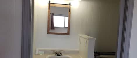 A bathroom with a sink, mirror, and toilet. There is a trash can and a towel hanging on the wall.