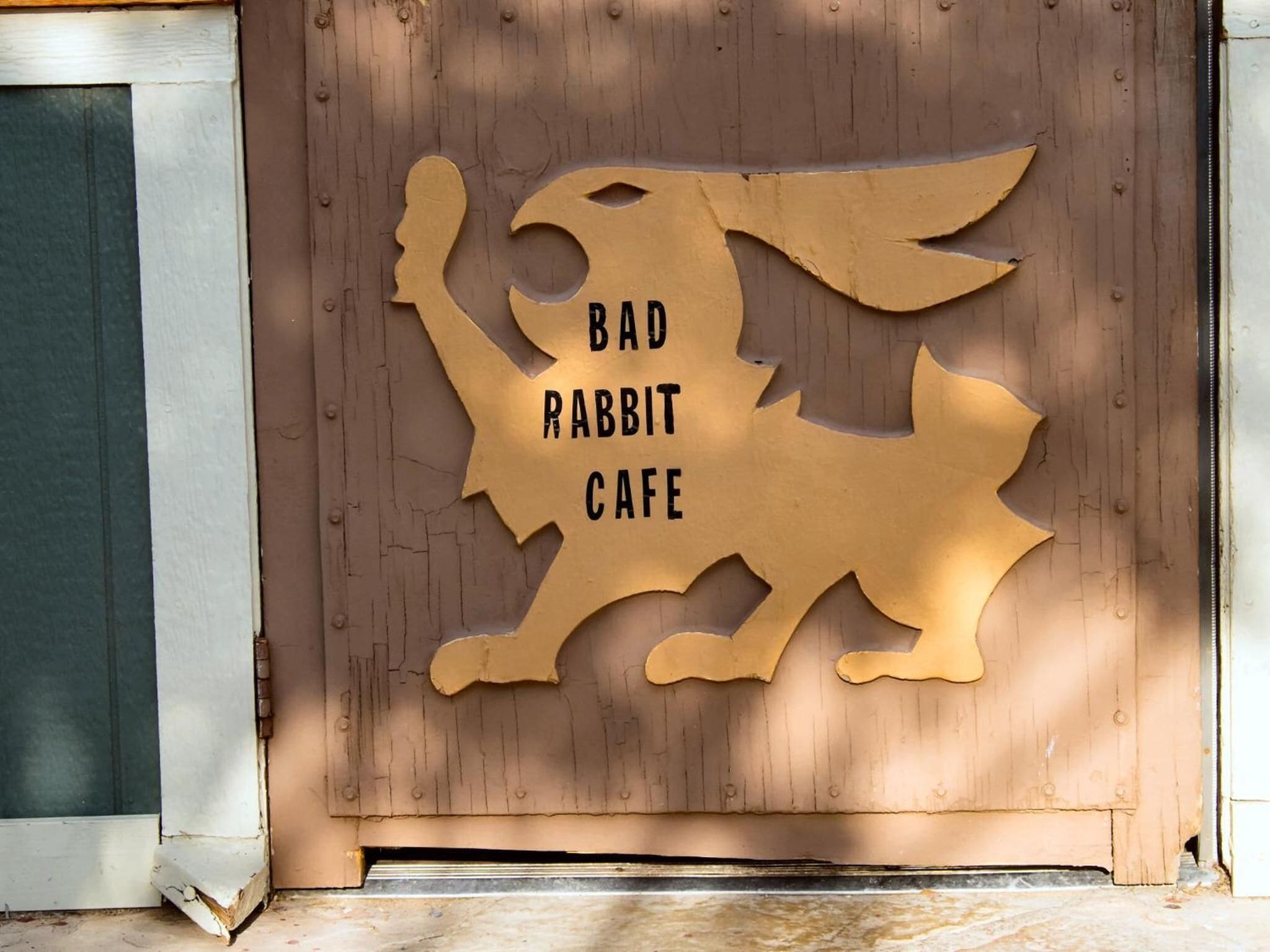 Une porte en bois avec une enseigne découpée qui porte l'inscription « BAD RABBIT CAFE ».