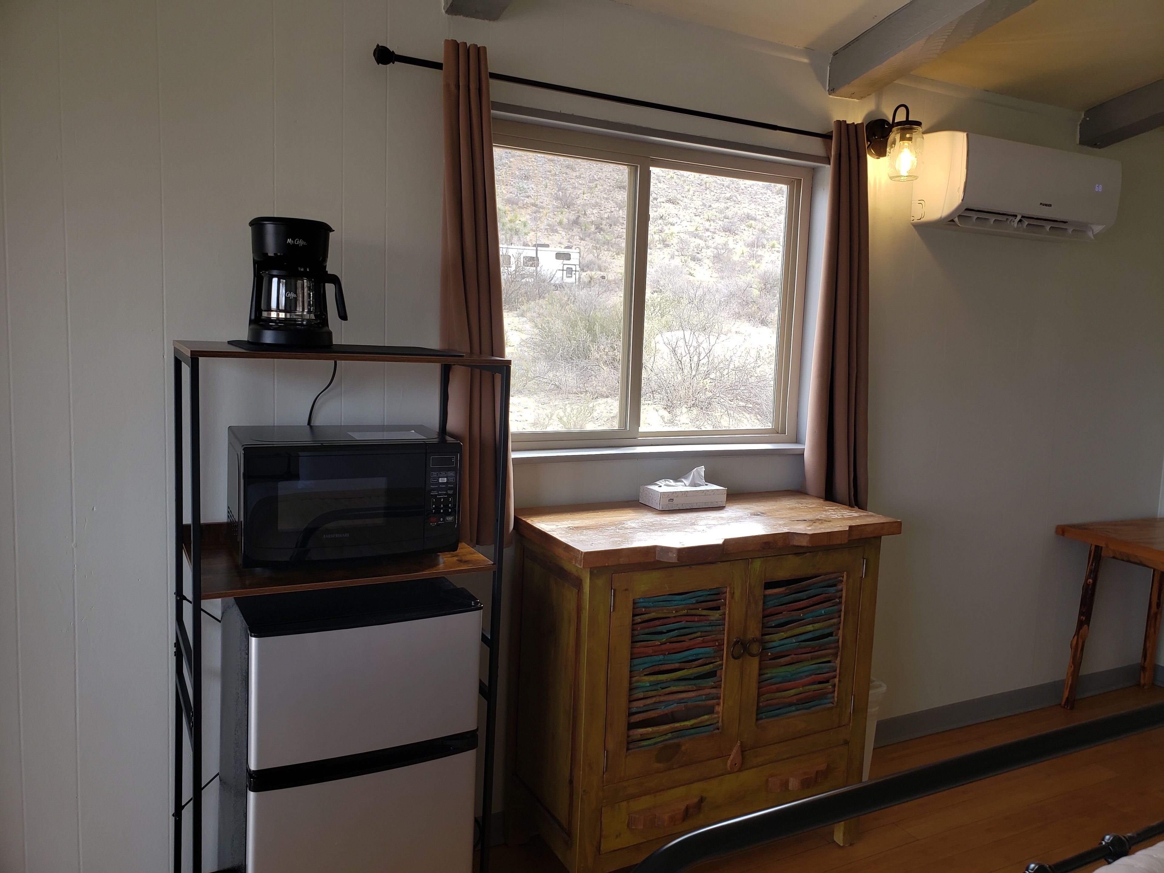 A compact kitchen with a microwave, coffee maker, and wooden cabinet with colorful slats.