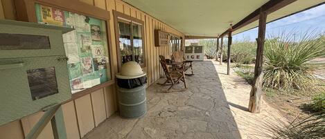 A covered outdoor area with a stone floor, wooden furniture, a trash bin, and a sign for an ice machine.