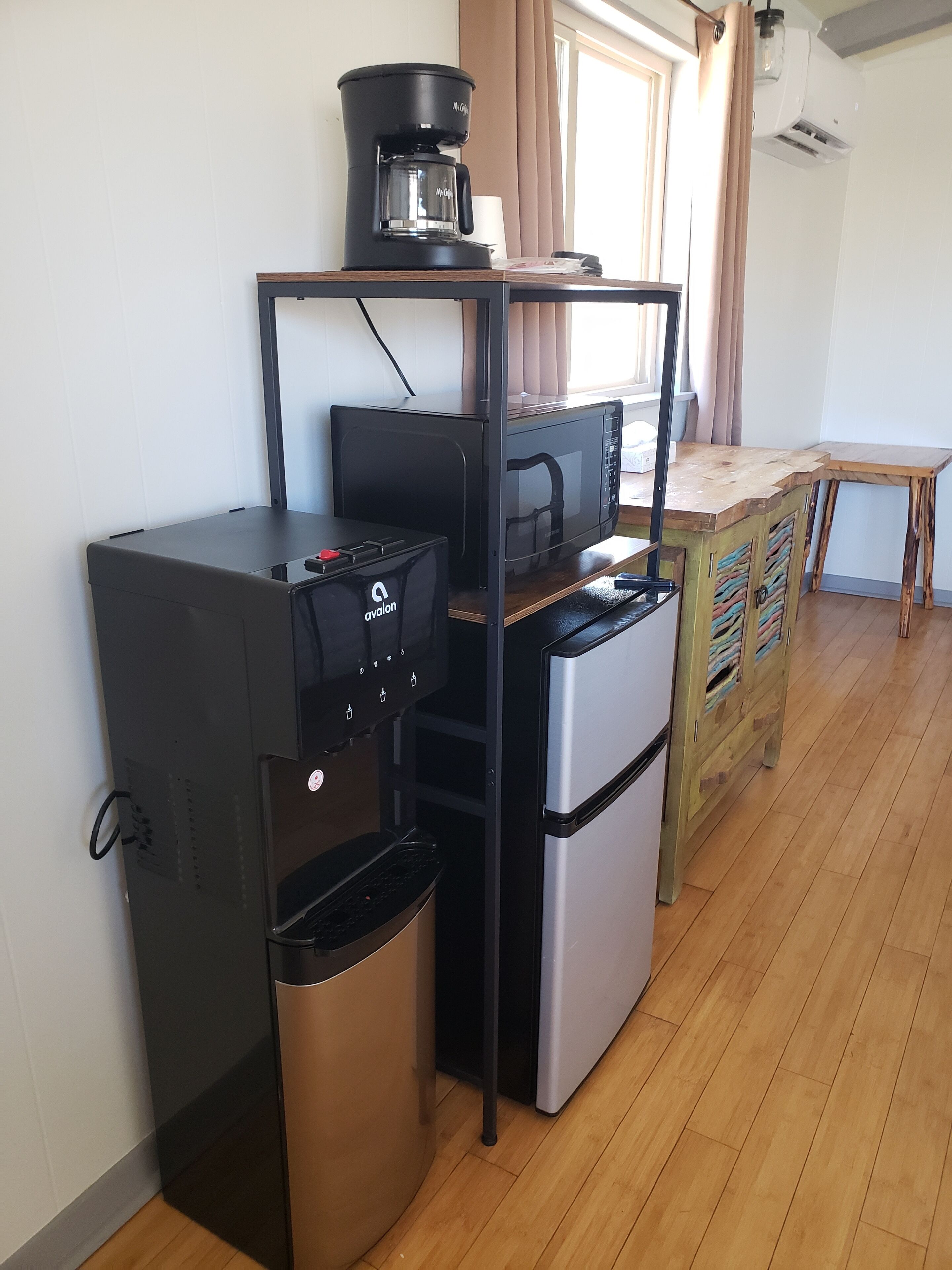 A compact kitchenette with a coffee maker, microwave, mini-fridge, and trash bin.