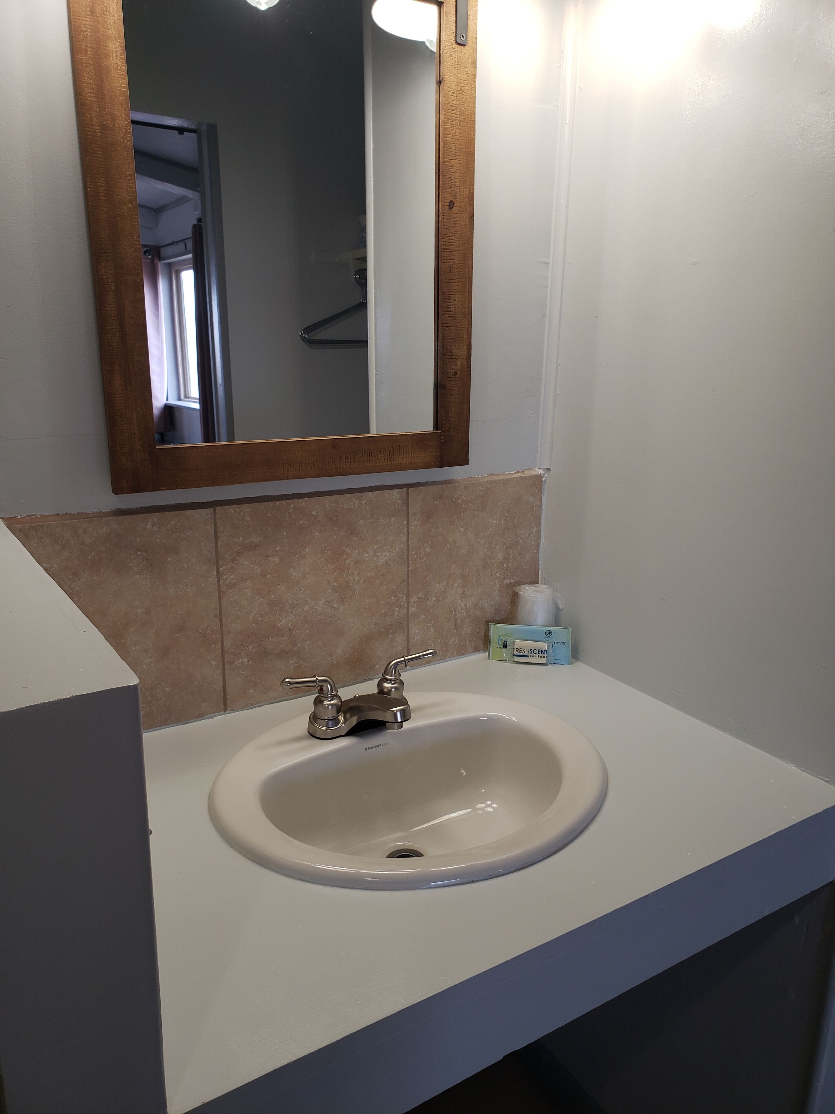 A bathroom with a white sink, a mirror with a wooden frame, and a towel dispenser.