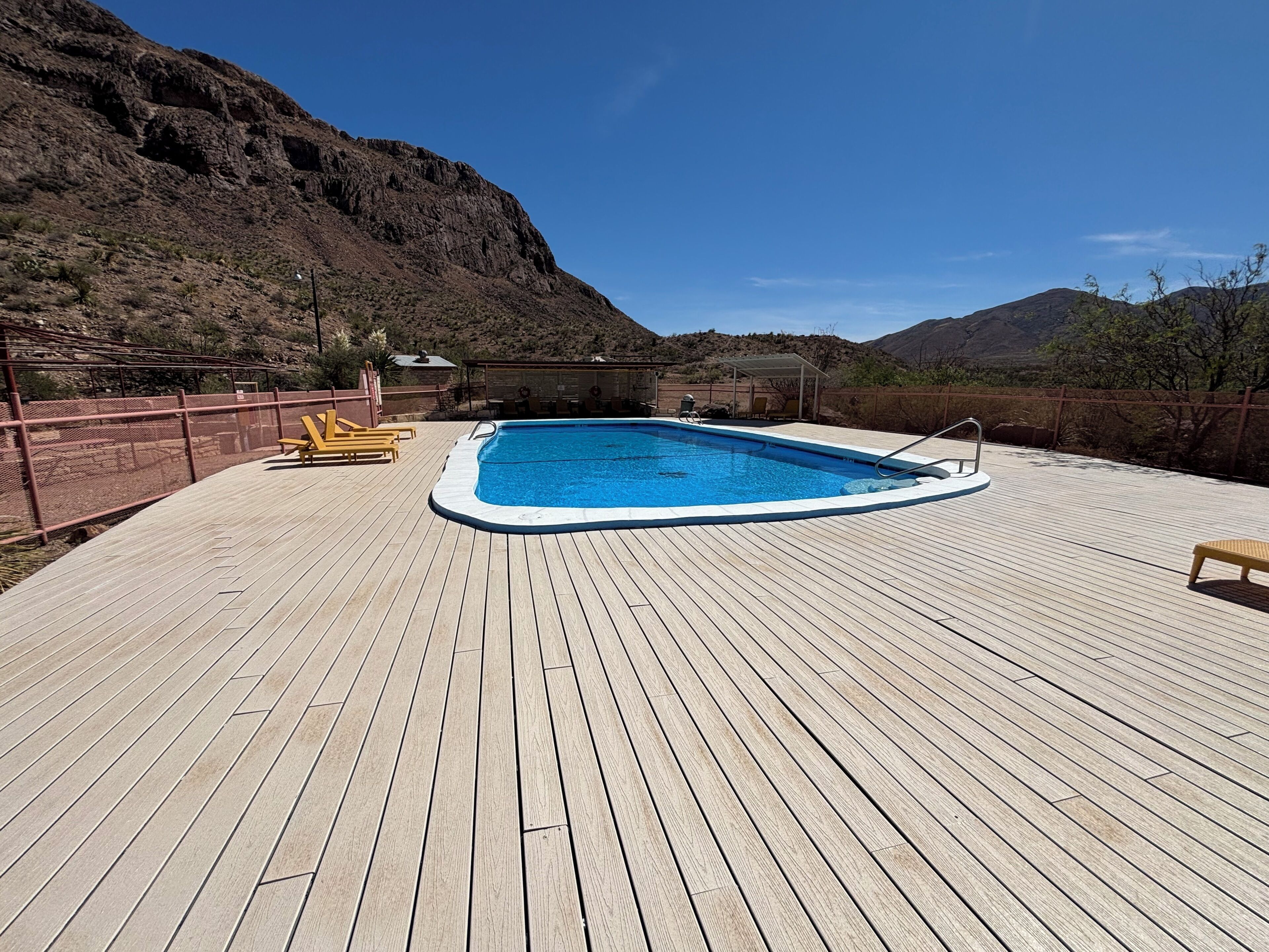 Um deck de madeira com piscina, espreguiçadeiras e área coberta.