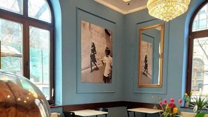 A café with a blue wall, a chandelier, and artwork. There is a cup of coffee on a saucer. - Atrium Hotel Ateneu City Center (Bucharest)