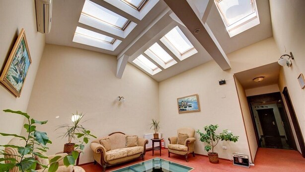 A spacious room with a high ceiling, skylights, a glass coffee table, and several pieces of furniture including sofas and chairs. - Atrium Hotel Ateneu City Center (Bucharest)