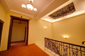 Un pasillo con piso alfombrado, una escalera con barandillas de metal decoradas y un candelabro en el techo.