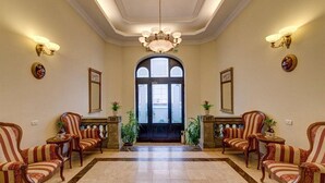 A lobby with a grand chandelier, two symmetrical seating areas with armchairs and side tables, a large arched doorway, and wall-mounted light fixtures. - Atrium Hotel Ateneu City Center (Bucharest)