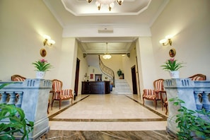 A spacious lobby with a marble floor, a grand staircase, and a reception desk.