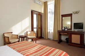 Habitación de hotel con una cama grande, dos sillas, un escritorio con televisor y un espejo.