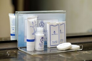 Una encimera de baño con artículos de aseo, incluyendo una botella, un tubo, una caja y dos pastillas de jabón.