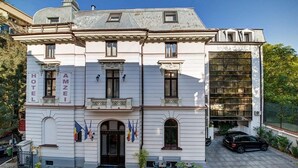 A white building with "HOTEL AMZEI" signage, a black car parked in front, and a balcony with flags. - Atrium Hotel Ateneu City Center (Bucharest)
