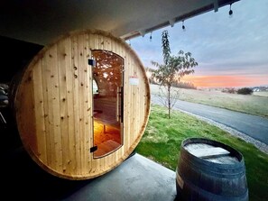 A wooden cabin with a circular door, a small window, and a view of a road and fields. - 4 Seasons Flathead Getaway - Hot Tub & Sauna! (Kalispell)