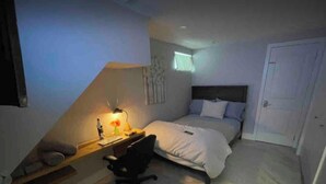 Een slaapkamer met een bed, bureau, stoel en een deur.