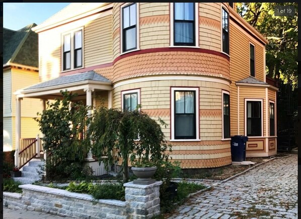 A two-story house with a curved facade, a front porch, and a stone pathway leading to the entrance. - Victorian house, clean comfortable and well located (Boston)