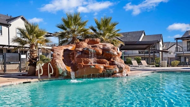 Una piscina con una cascada de roca, rodeada de palmeras y casas modernas.