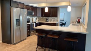 Una cocina moderna con armarios de madera oscura, electrodomésticos de acero inoxidable, una isla grande con taburetes de bar e iluminación colgante.
